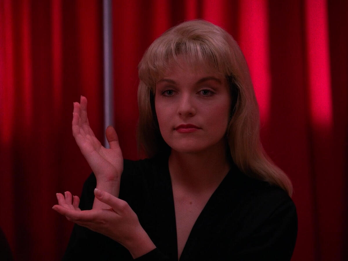 Laura Palmer from Twin Peaks doing a tree symbol with her arms.